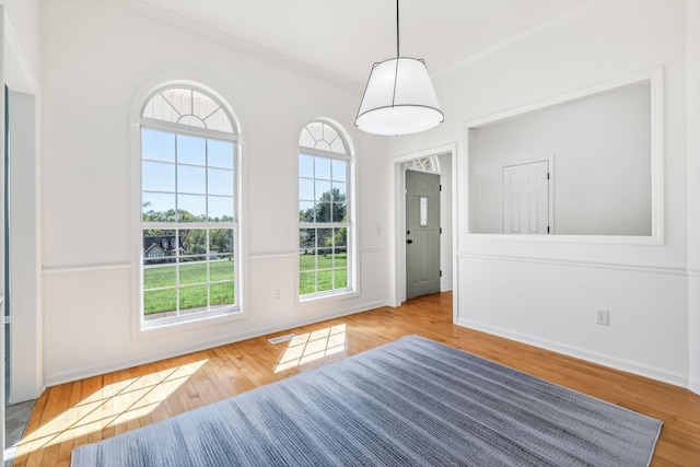 unfurnished dining area with a wealth of natural light, crown molding, and light wood-type flooring