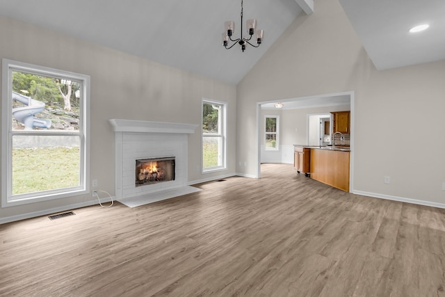 unfurnished living room with a chandelier, light wood-type flooring, high vaulted ceiling, and a healthy amount of sunlight