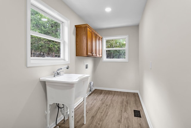 washroom featuring hookup for a washing machine, cabinets, plenty of natural light, and light hardwood / wood-style floors