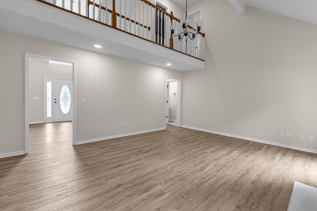 unfurnished living room with a notable chandelier, wood-type flooring, and a towering ceiling