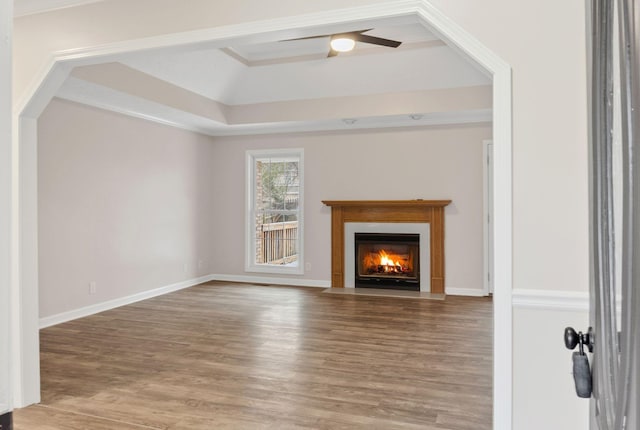 unfurnished living room with hardwood / wood-style flooring, a raised ceiling, and ceiling fan