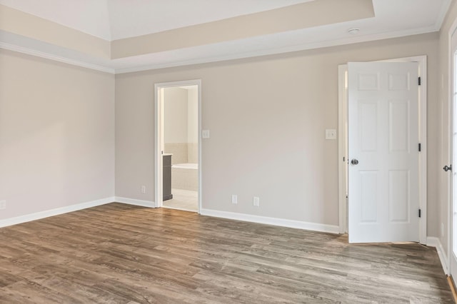 empty room featuring a tray ceiling, hardwood / wood-style floors, and ornamental molding