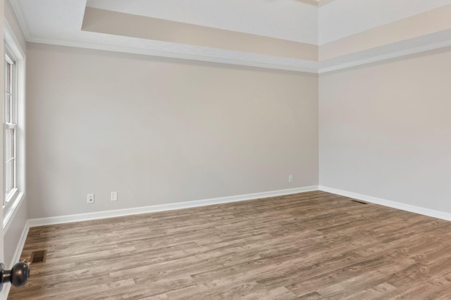 empty room with hardwood / wood-style floors, a raised ceiling, a wealth of natural light, and crown molding