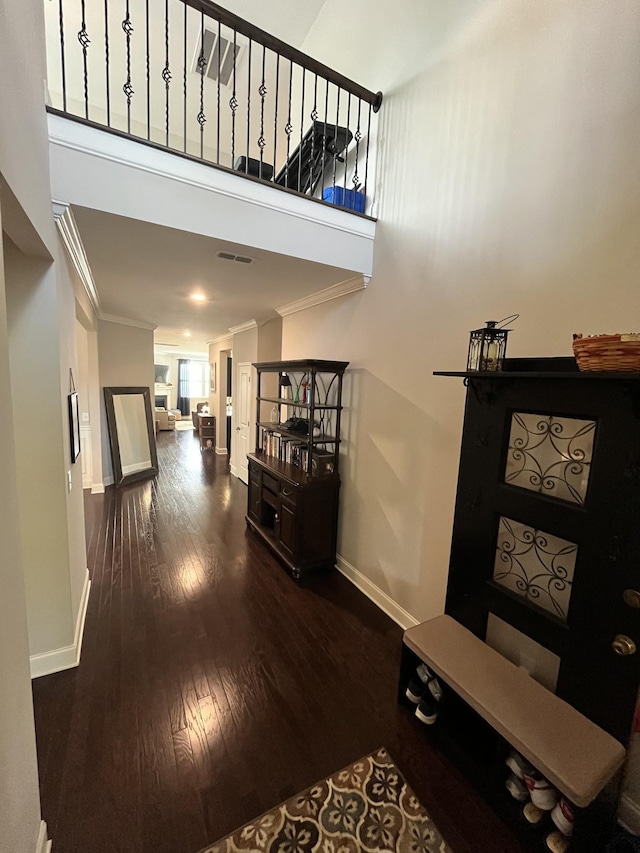 hall with a towering ceiling, dark hardwood / wood-style floors, and ornamental molding