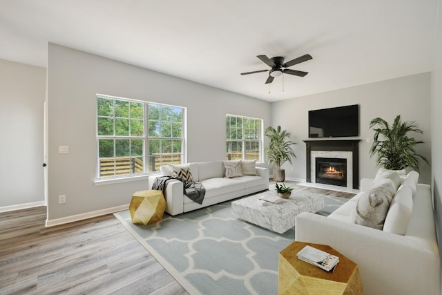 living room with a high end fireplace, ceiling fan, and light wood-type flooring