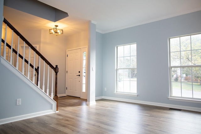 foyer featuring hardwood / wood-style flooring, crown molding, a wealth of natural light, and a chandelier