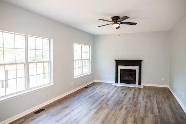 unfurnished living room with ceiling fan, a high end fireplace, and light wood-type flooring