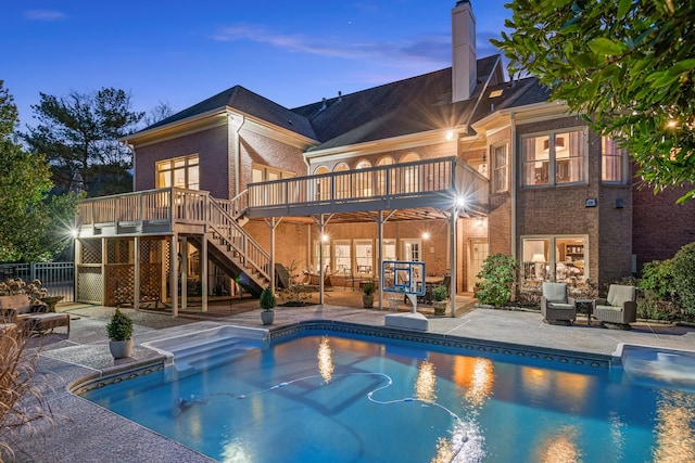 pool at dusk with a wooden deck and a patio area