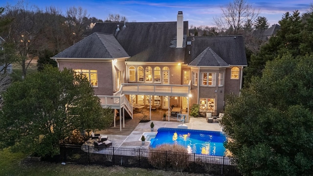 back house at dusk featuring a fenced in pool, a patio, a balcony, and outdoor lounge area