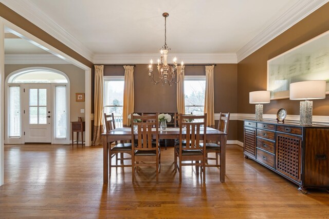 dining area with a notable chandelier, crown molding, dark wood-type flooring, and plenty of natural light