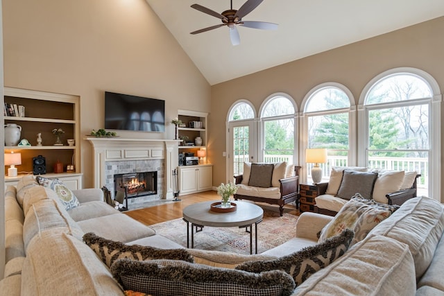 living room featuring a healthy amount of sunlight, a fireplace, high vaulted ceiling, and light wood-type flooring