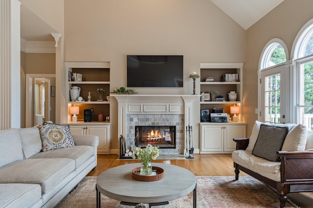 living room featuring high vaulted ceiling, built in features, a fireplace, and light hardwood / wood-style flooring