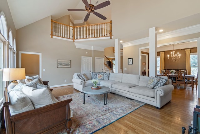 living room with ceiling fan with notable chandelier, ornamental molding, wood-type flooring, and high vaulted ceiling