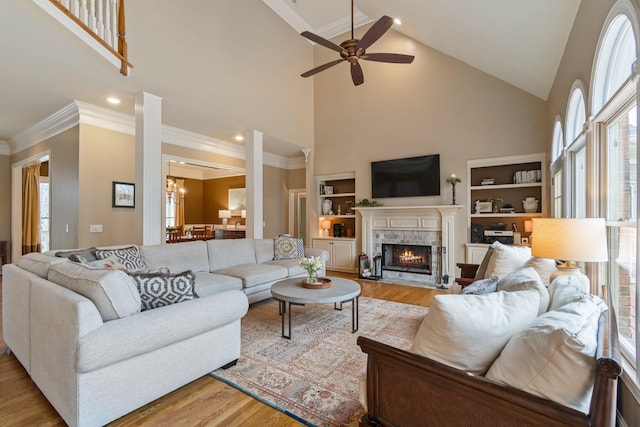 living room with crown molding, high vaulted ceiling, a tile fireplace, and light hardwood / wood-style flooring