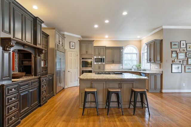 kitchen featuring crown molding, built in appliances, a center island, and light hardwood / wood-style flooring