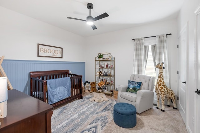 bedroom featuring ceiling fan, a nursery area, and light carpet