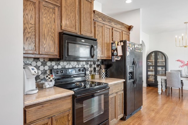 kitchen with light wood-type flooring, backsplash, black appliances, a notable chandelier, and hanging light fixtures