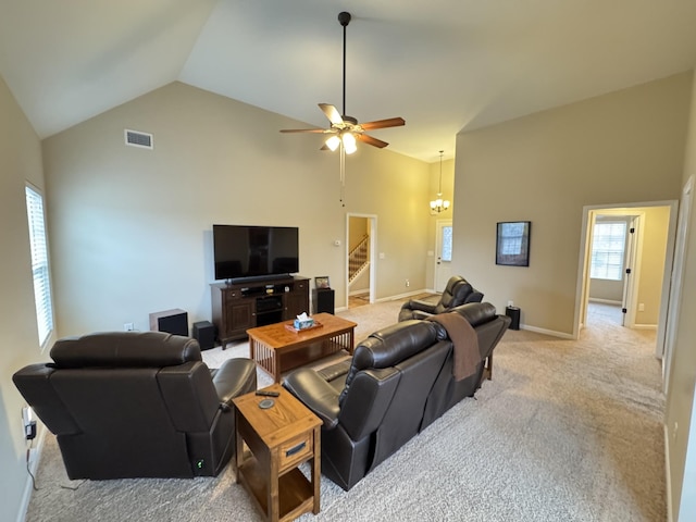 carpeted living room with high vaulted ceiling and ceiling fan with notable chandelier