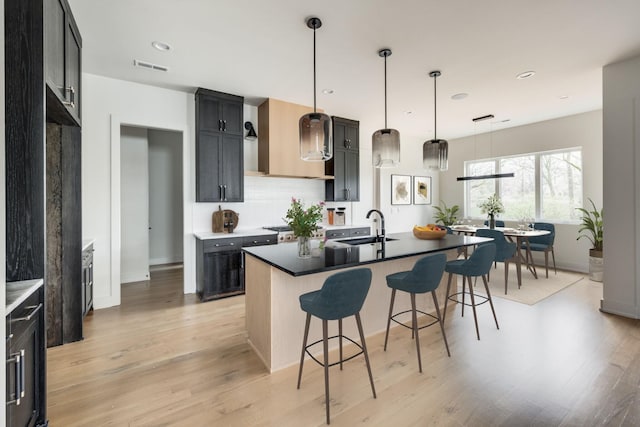 kitchen with sink, hanging light fixtures, wall chimney range hood, a breakfast bar, and a center island with sink