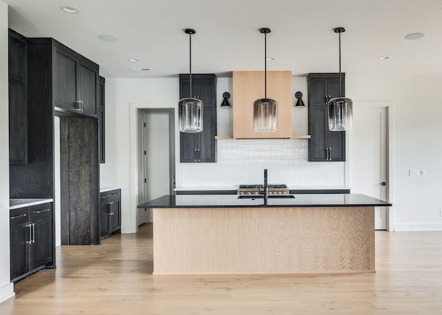 kitchen featuring backsplash, a center island with sink, light hardwood / wood-style floors, and sink