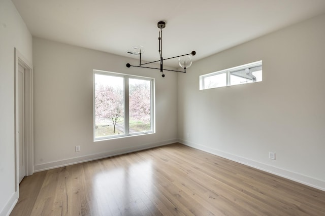 empty room featuring a notable chandelier and light wood-type flooring