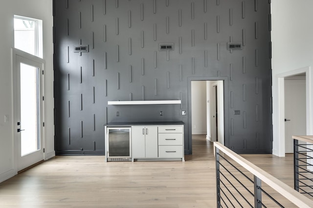 kitchen with wine cooler, light wood-type flooring, white cabinetry, and a towering ceiling