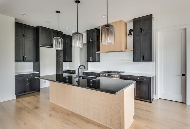 kitchen with light wood-type flooring, a kitchen island with sink, sink, decorative light fixtures, and range hood