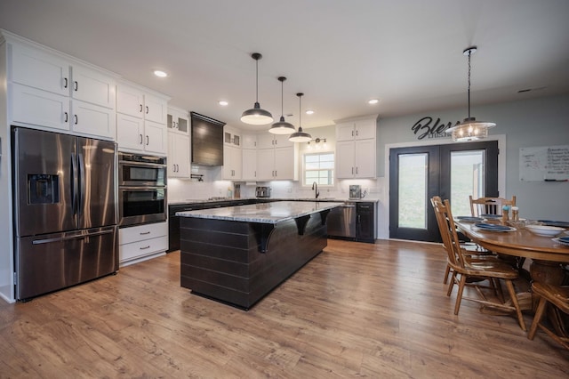 kitchen featuring white cabinetry, light stone counters, decorative light fixtures, a kitchen island, and appliances with stainless steel finishes