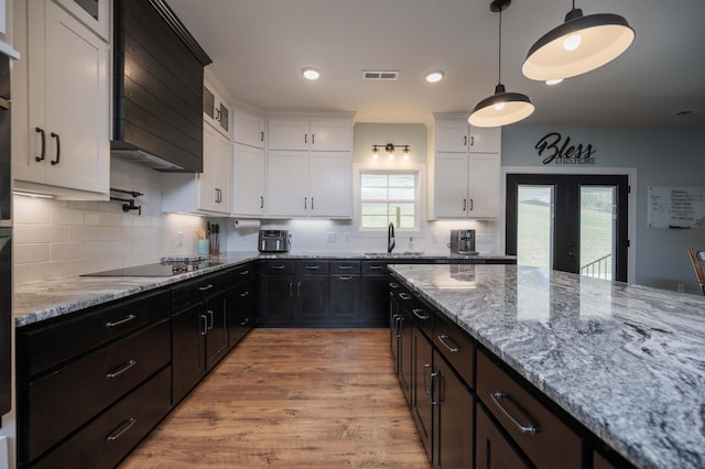 kitchen with black electric cooktop, sink, light hardwood / wood-style flooring, white cabinets, and hanging light fixtures