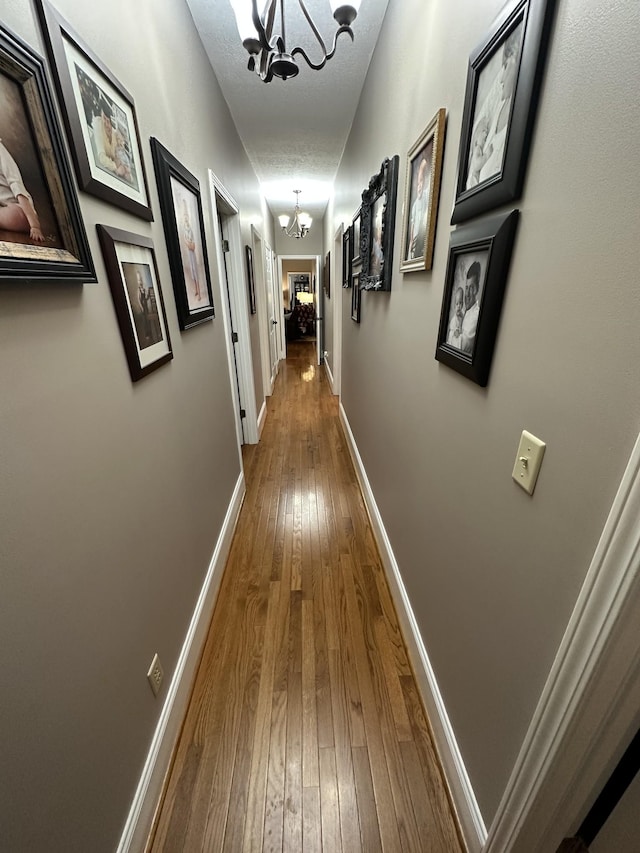 corridor with wood-type flooring, a textured ceiling, and an inviting chandelier