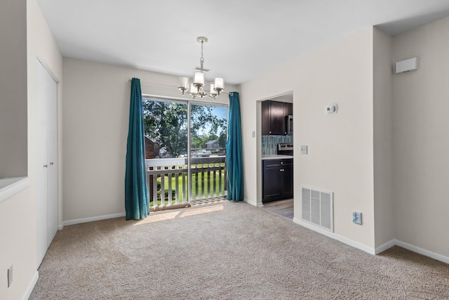 empty room with light colored carpet and an inviting chandelier