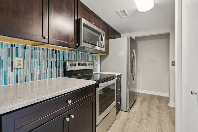 kitchen with decorative backsplash, stainless steel appliances, light stone countertops, dark brown cabinets, and light hardwood / wood-style flooring