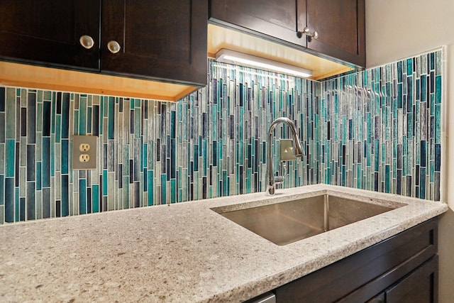 kitchen featuring light stone counters, sink, backsplash, and dark brown cabinets