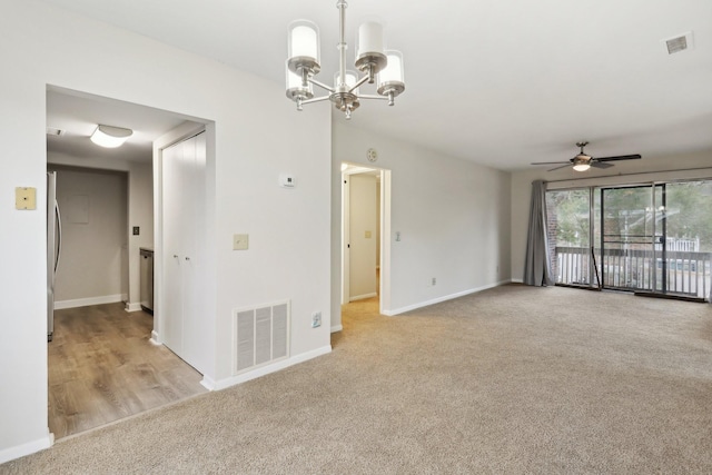 carpeted spare room featuring ceiling fan with notable chandelier