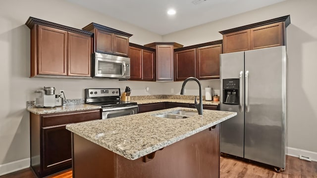 kitchen with appliances with stainless steel finishes, light stone counters, sink, light hardwood / wood-style flooring, and an island with sink