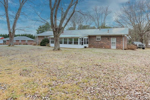 back of property featuring a sunroom, brick siding, a yard, and metal roof