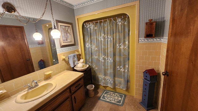 full bath with wallpapered walls, wainscoting, curtained shower, vanity, and tile walls