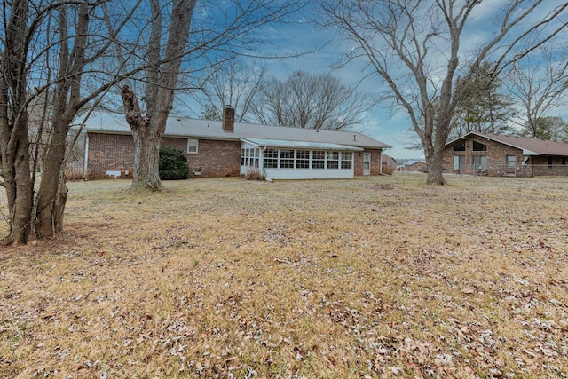 back of house featuring a yard, brick siding, a chimney, and a sunroom