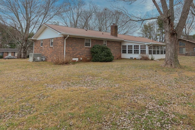 back of house with central AC unit, brick siding, a sunroom, a yard, and a chimney