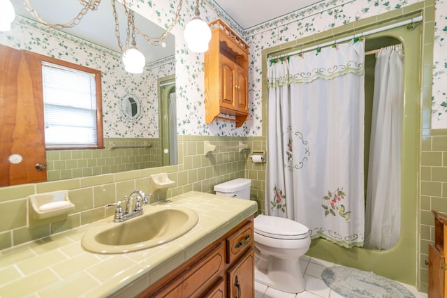 bathroom with toilet, wallpapered walls, vanity, and wainscoting