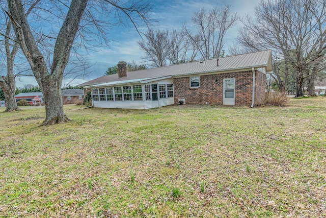 rear view of house with a lawn, a sunroom, a chimney, metal roof, and brick siding