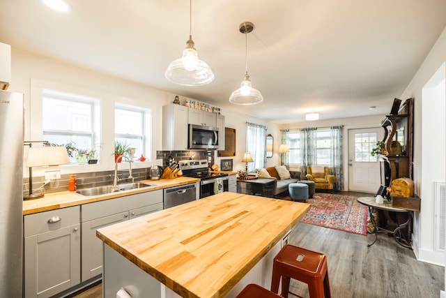 kitchen with butcher block counters, sink, stainless steel appliances, pendant lighting, and gray cabinets