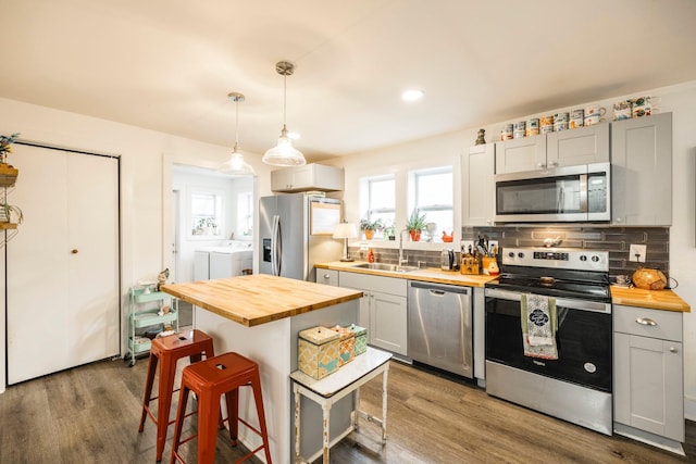 kitchen with washer and clothes dryer, a kitchen breakfast bar, stainless steel appliances, wood counters, and a sink