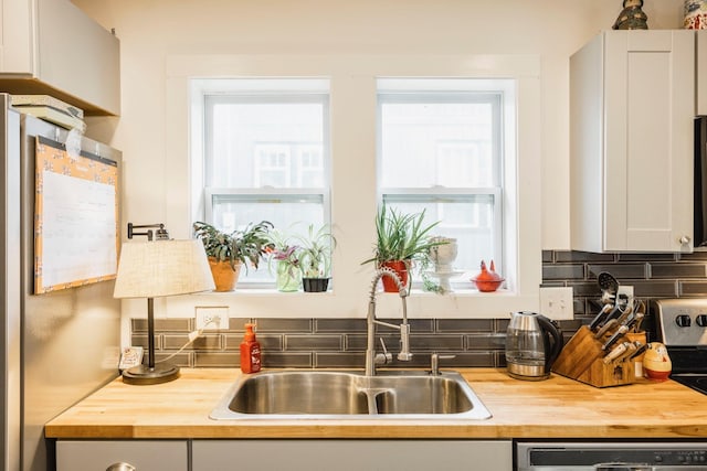 kitchen with backsplash, butcher block countertops, dishwashing machine, and a sink