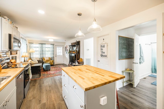 kitchen featuring wooden counters, appliances with stainless steel finishes, decorative light fixtures, a kitchen island, and white cabinetry