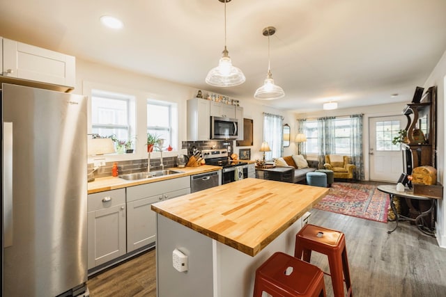 kitchen with a breakfast bar area, dark wood-style flooring, a sink, appliances with stainless steel finishes, and wood counters