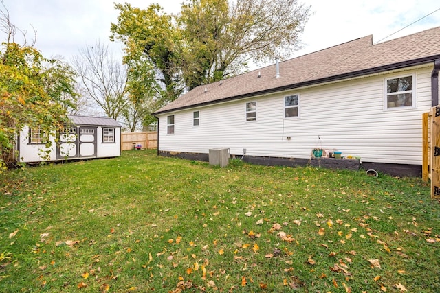 back of house with a storage unit, an outbuilding, fence, a yard, and roof with shingles