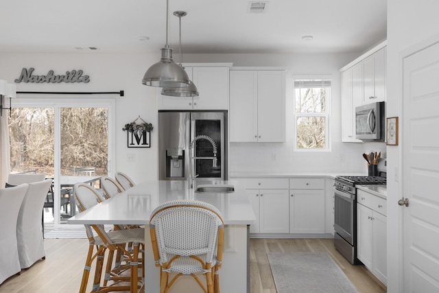 kitchen with decorative backsplash, light wood-type flooring, stainless steel appliances, pendant lighting, and white cabinetry