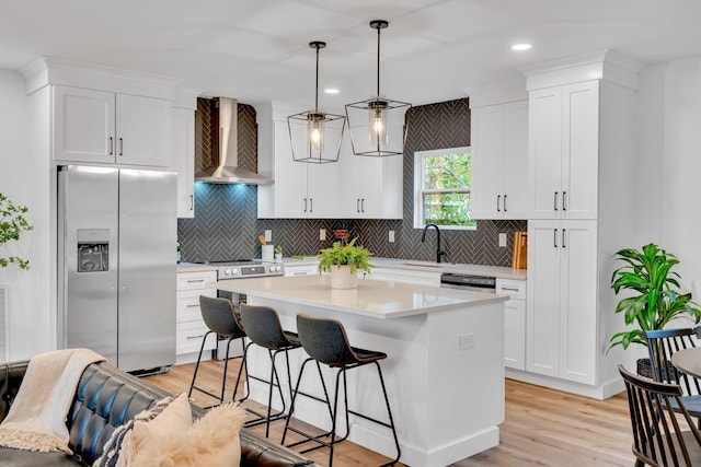 kitchen with hanging light fixtures, wall chimney exhaust hood, stainless steel fridge, a kitchen island, and white cabinetry