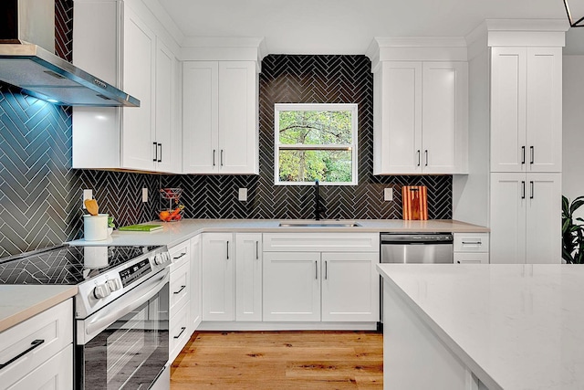 kitchen featuring white cabinetry, wall chimney range hood, sink, and appliances with stainless steel finishes